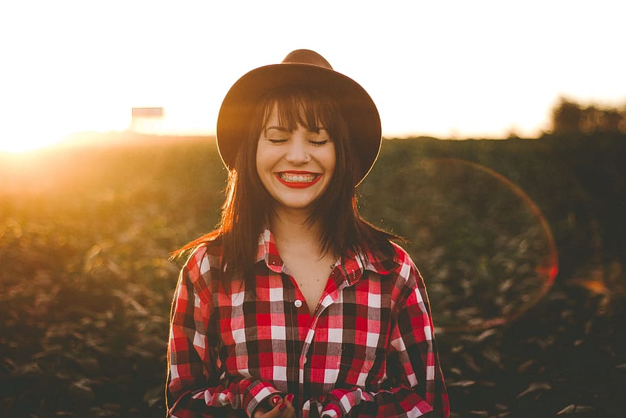 golden hour photography of woman in red and white checkered dress shirt, woman smiling while standing surrounded by plants during golden hour