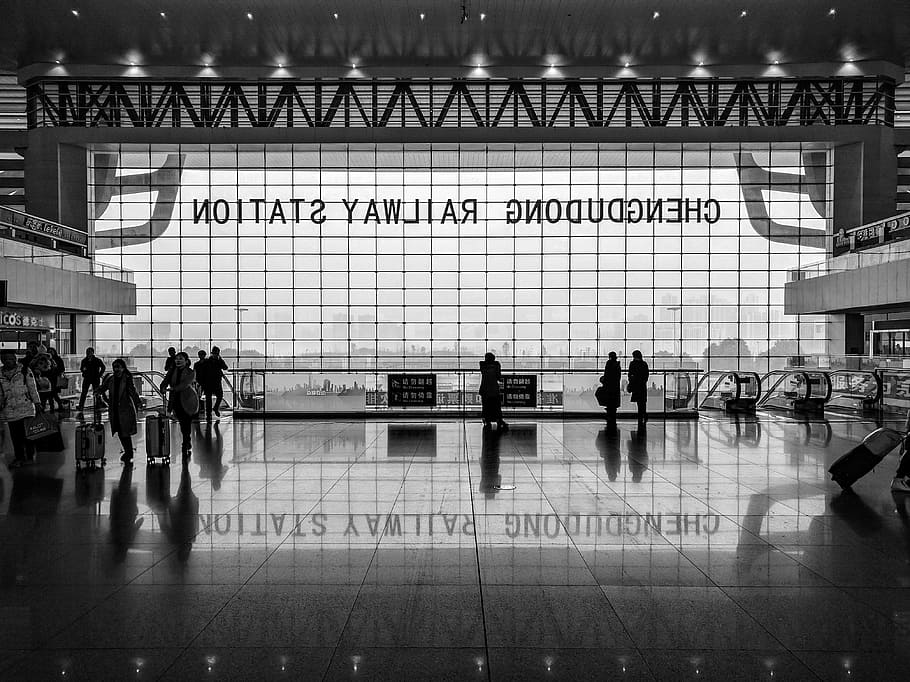 Black and white shot of station foyer with people and large window and reflection on floor, grayscale photo of airport interior