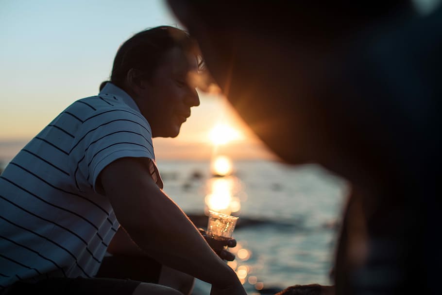 Summer in the Swedish archipelago, man holding drinking glass filled with liquid near body of water at daytime HD wallpaper
