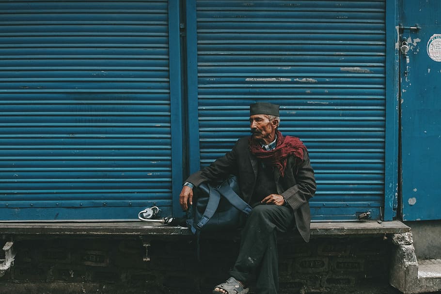 man sitting on gray bench in front of blue shutter door, man sitting on concrete bench in front of roller shutter door HD wallpaper
