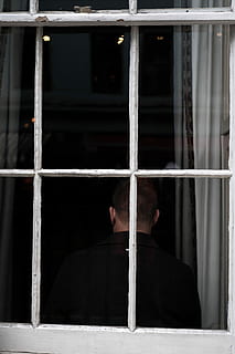 man standing front of glass window, man in black collared top sitting beside white framed clear glass window during daytime HD wallpaper
