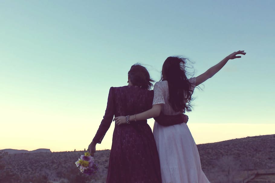 two women standing under the cliff during daytime, girlfriends
