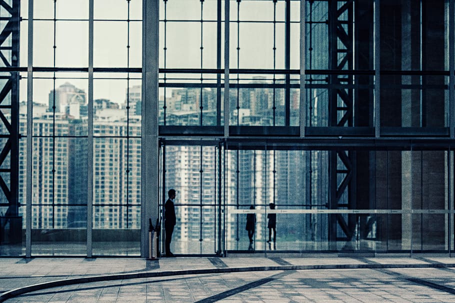 silhouette of man standing in front of curtain wall building, man standing beside the glass door of the building HD wallpaper