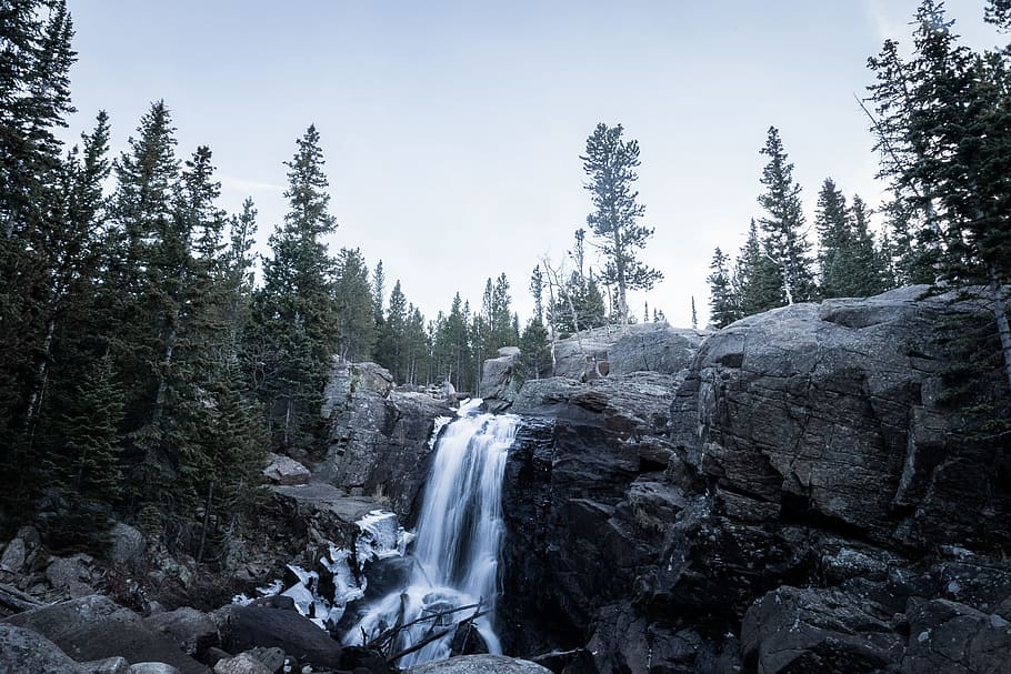 timelapse photography of waterfall surrounded by trees under blue sky at daytime, waterfalls surrounded with pine tree during daytime HD wallpaper