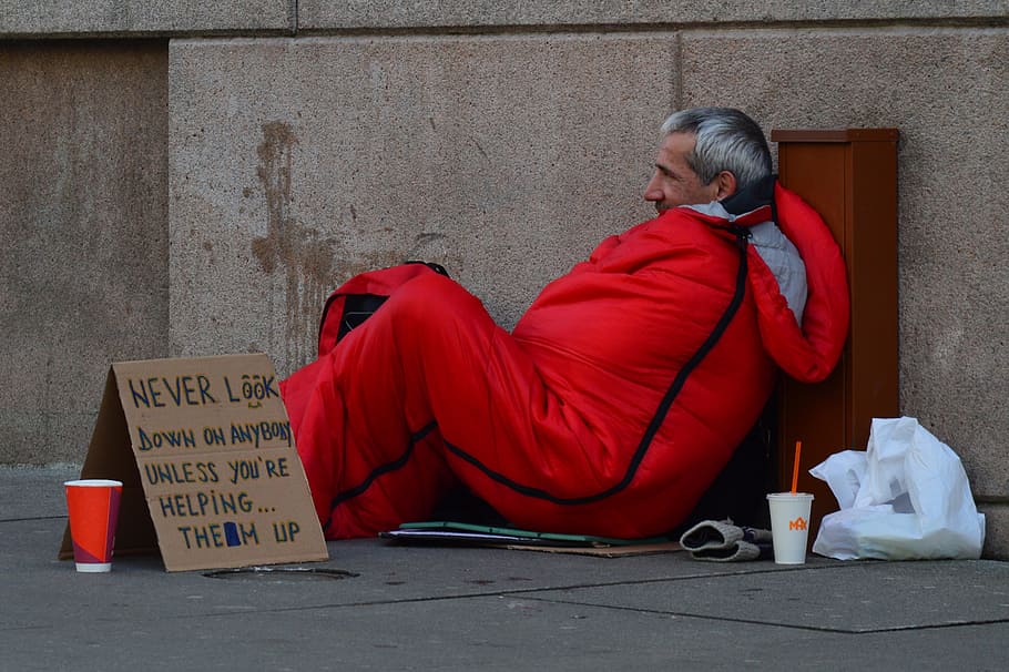 man in red sleeping bag beside brown cardboard box, homeless man