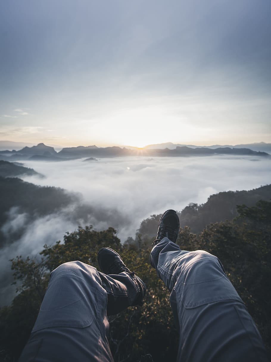person's feet facing foggy mountain field during golden hour, person above green tree during daytime HD wallpaper
