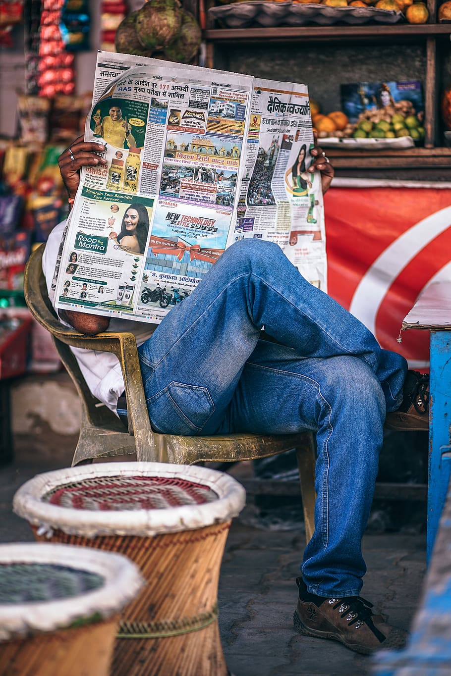 person reading newspaper sitting on armchair, tilt shift lens photography of man wearing blue jeans while holding newspaper, HD wallpaper