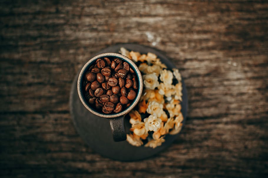 brown coffee beans on gray mug, cup filled with coffee beans beside flowers HD wallpaper