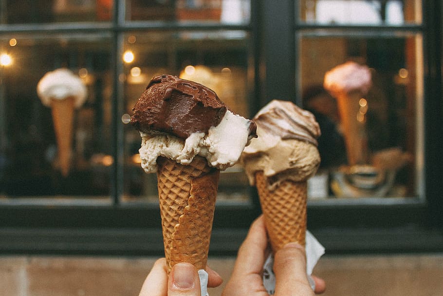 persons holding two chocolate ice creams, cone, mocha, vanilla