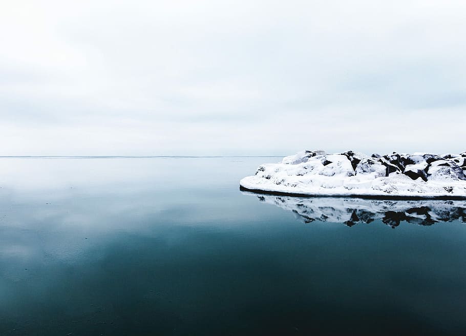 black rock formation covered with snow beside calm body of water, white snow on rock formation HD wallpaper