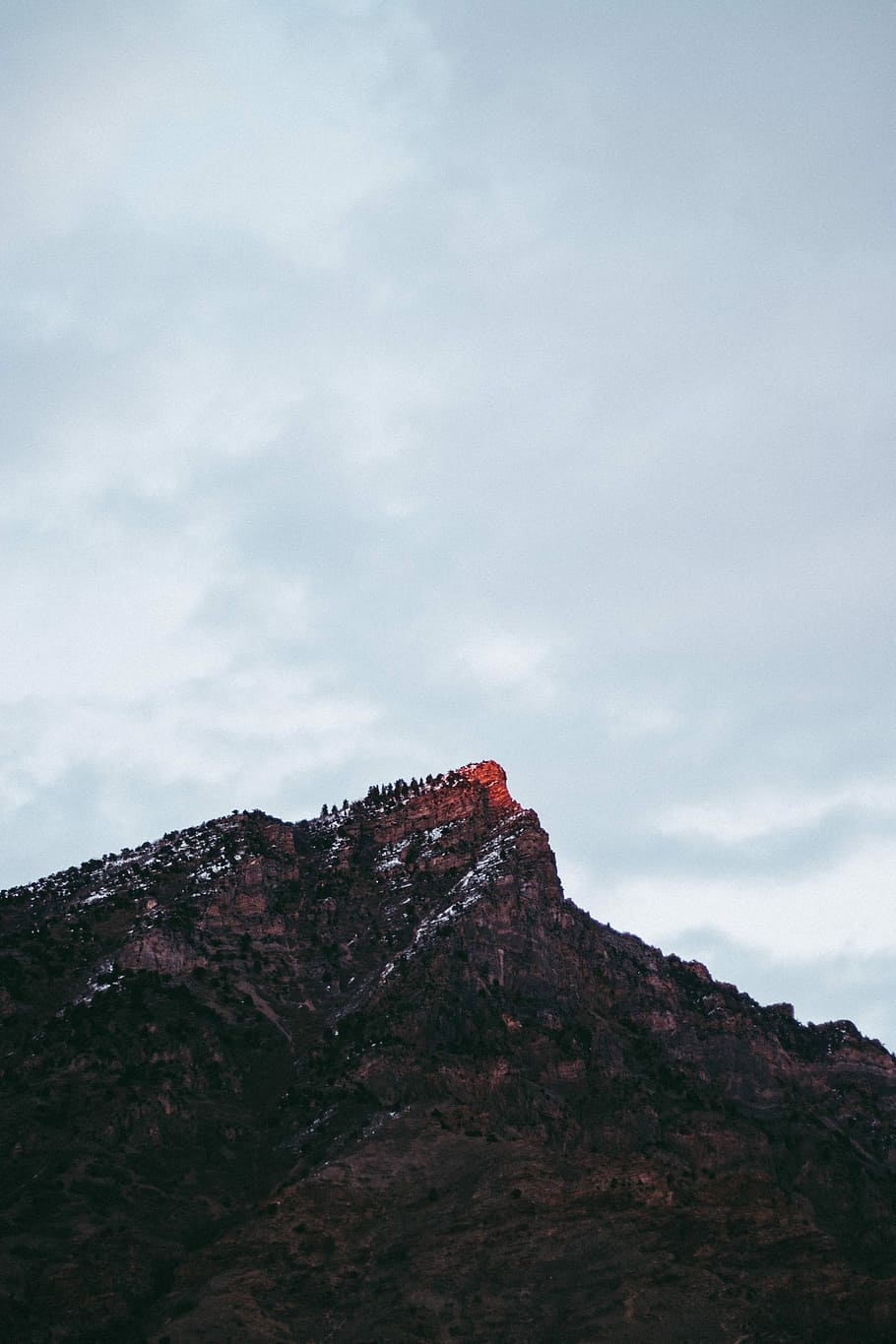 brown rocky mountain under gray sky, landscape photography of mountain covered trees HD wallpaper