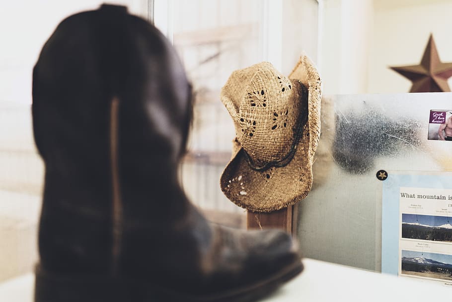 black cowboy boot near brown straw hat on white wall selective-focus photography, selective focus photography of brown cowboy hat hanged beside wall, HD wallpaper
