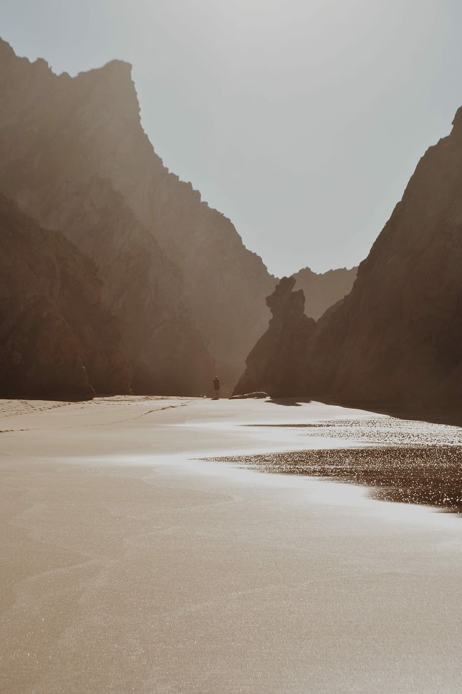 man walking near shore, person standing on body of water surrounded mountains HD wallpaper