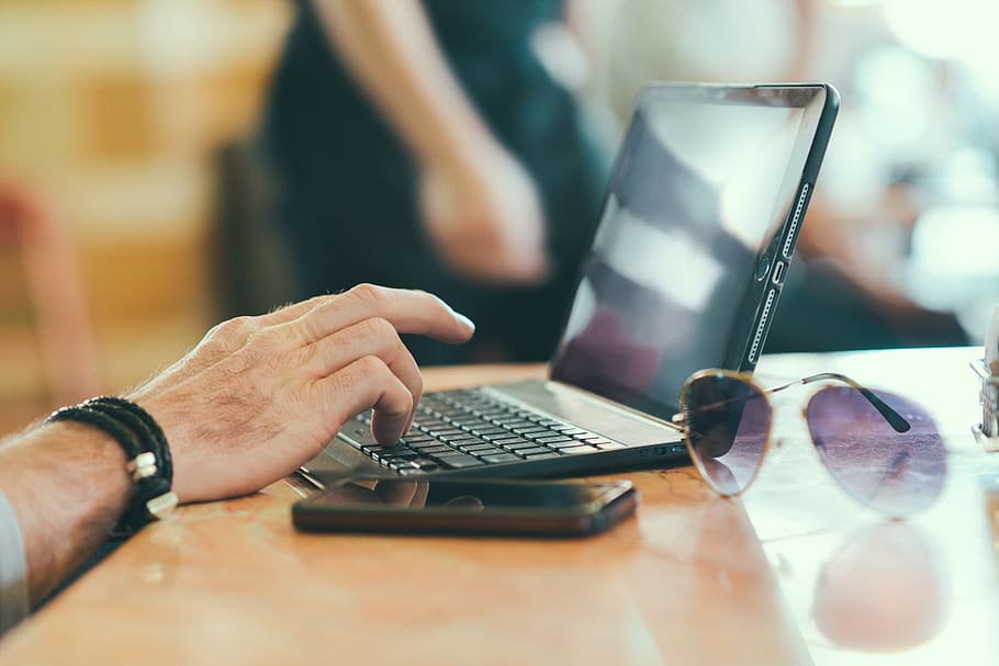 black laptop beside black smartphone and purple sunglasses with gold-colored frames on brown wooden desk HD wallpaper