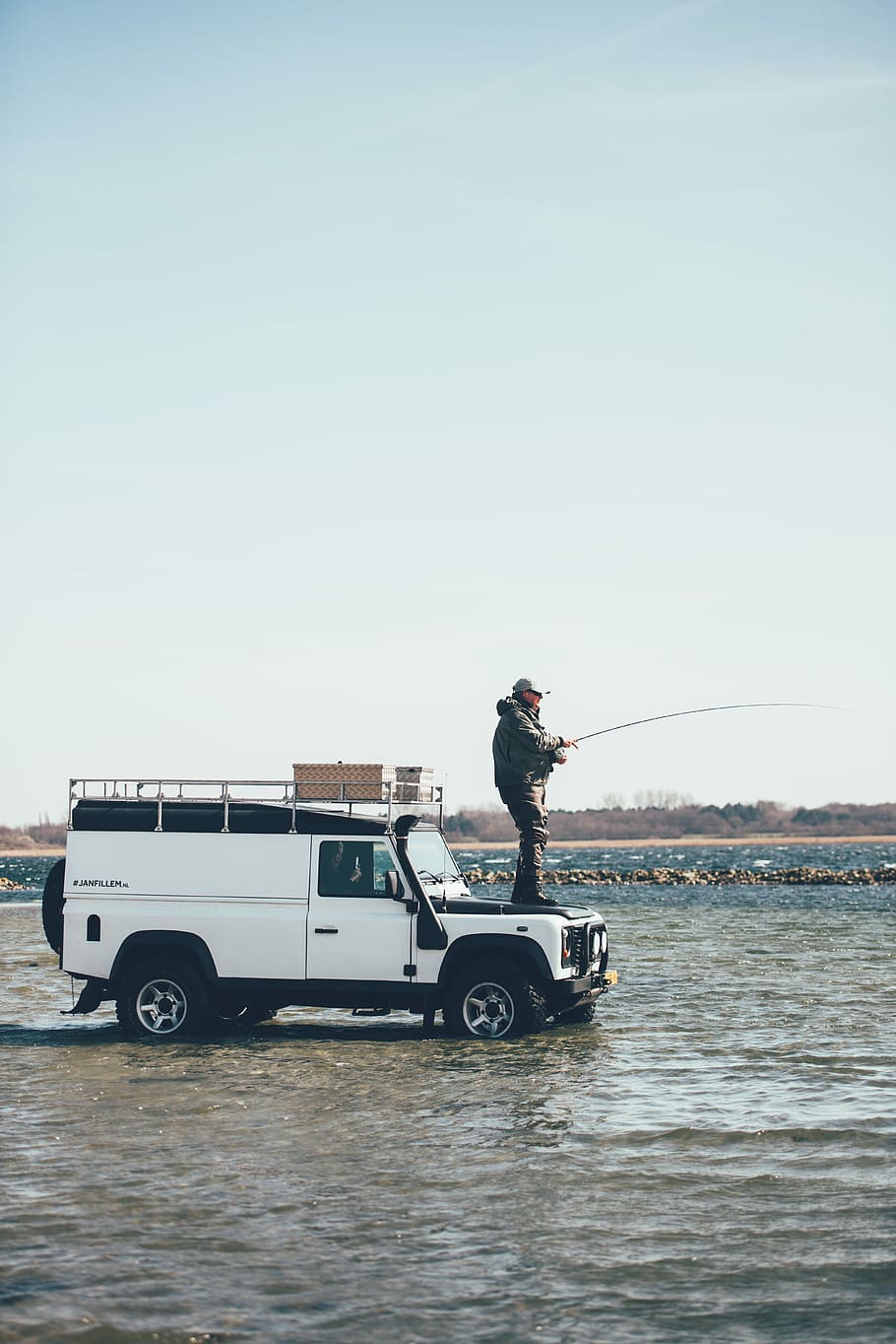 man holding fishing rod on SUV hood\, person fishing on top of white Land Rover SUV