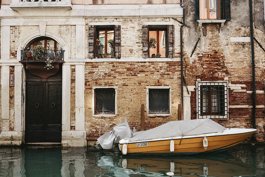 orange boat in front of building, brown and white speedboat on body of water next to concrete building HD wallpaper
