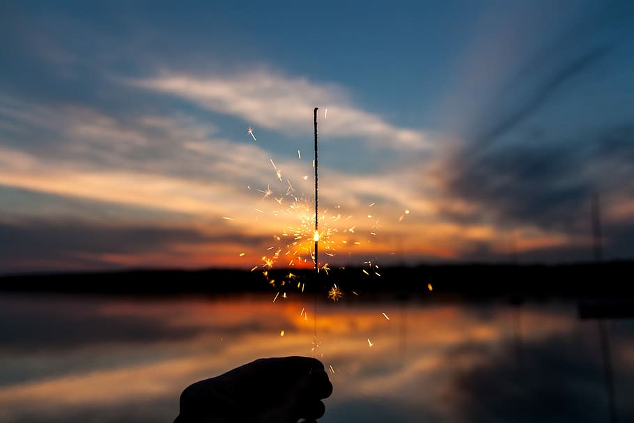 silhouette of person holding sparker, person holding sparkler overlooking body of water and sunset HD wallpaper