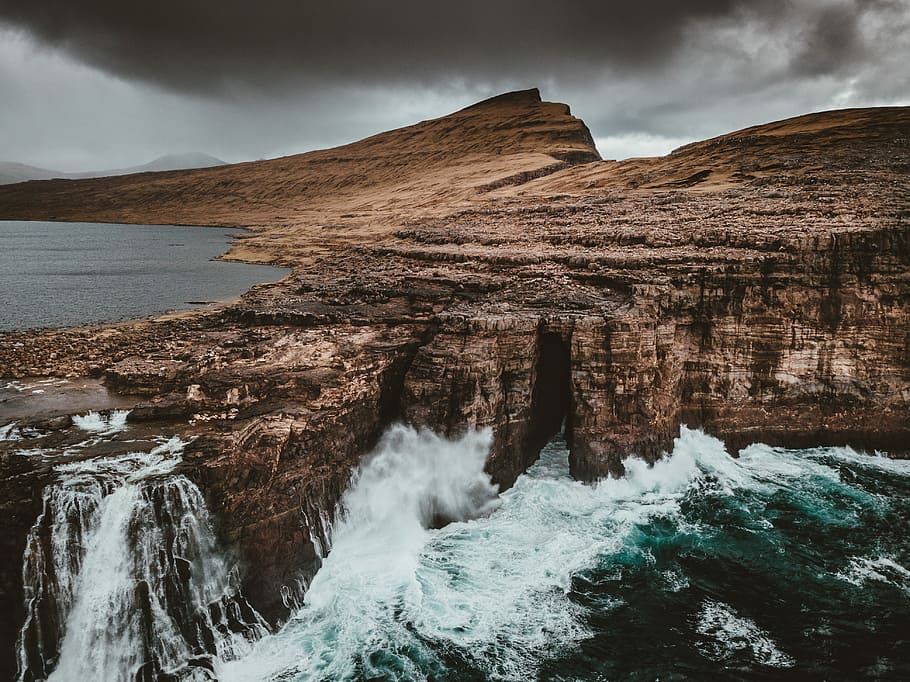 tidal waved into cliff, photo of brown mountain near body of water HD wallpaper