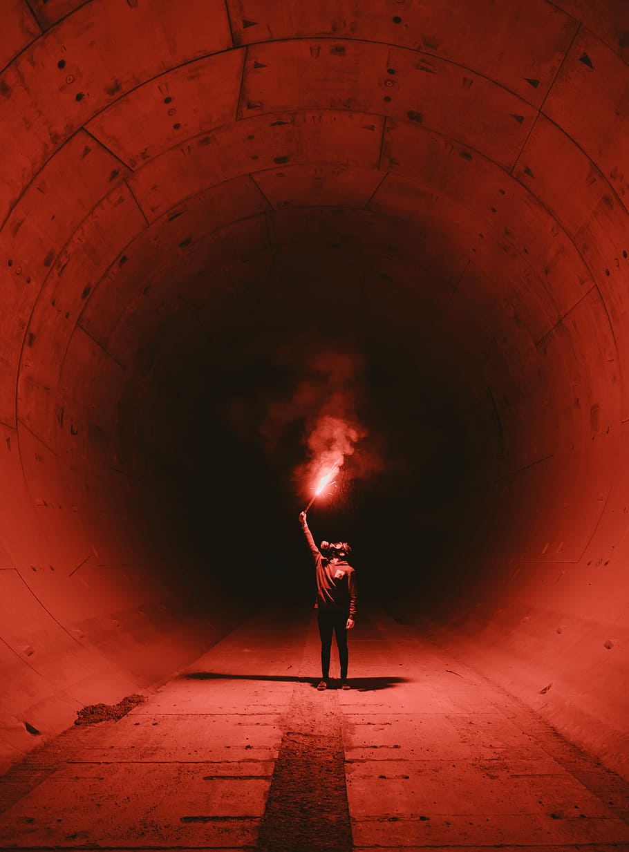 man wearing gas mask holding torch inside tunnel, human in the tunnel holding red light