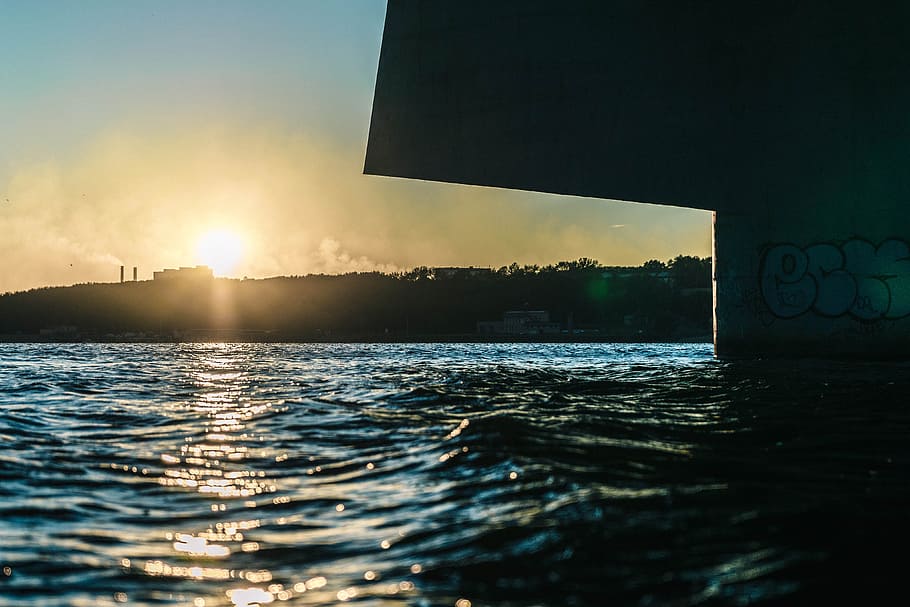 low angle photography of sun behind building on hill over the sea, landscape photo of body of water during golden hour HD wallpaper