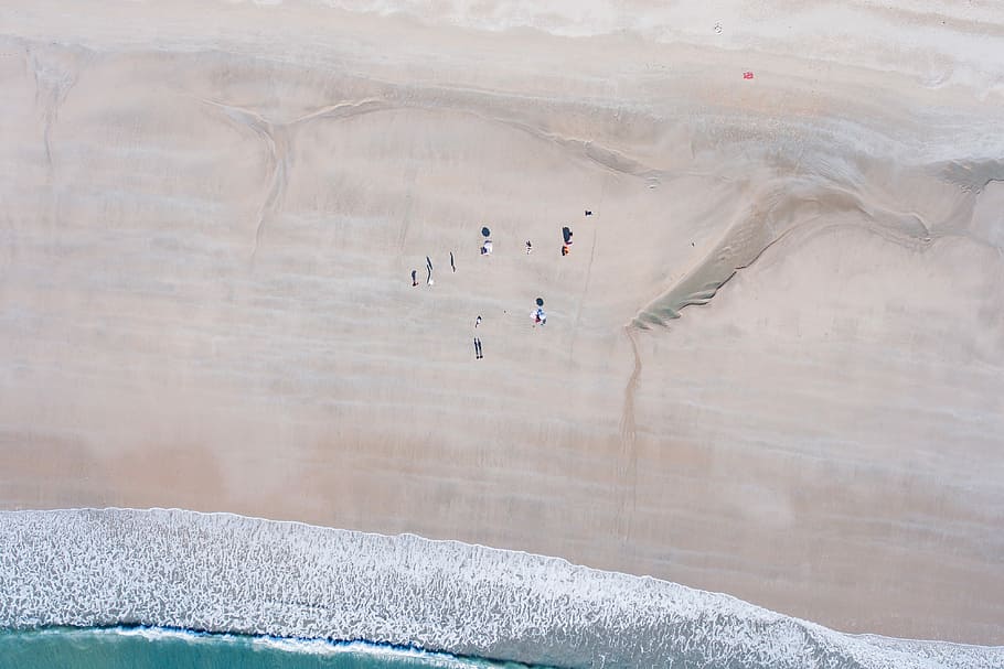 aerial view of group of people standing next to blue ocean water, aerial photography of sand near body of water HD wallpaper