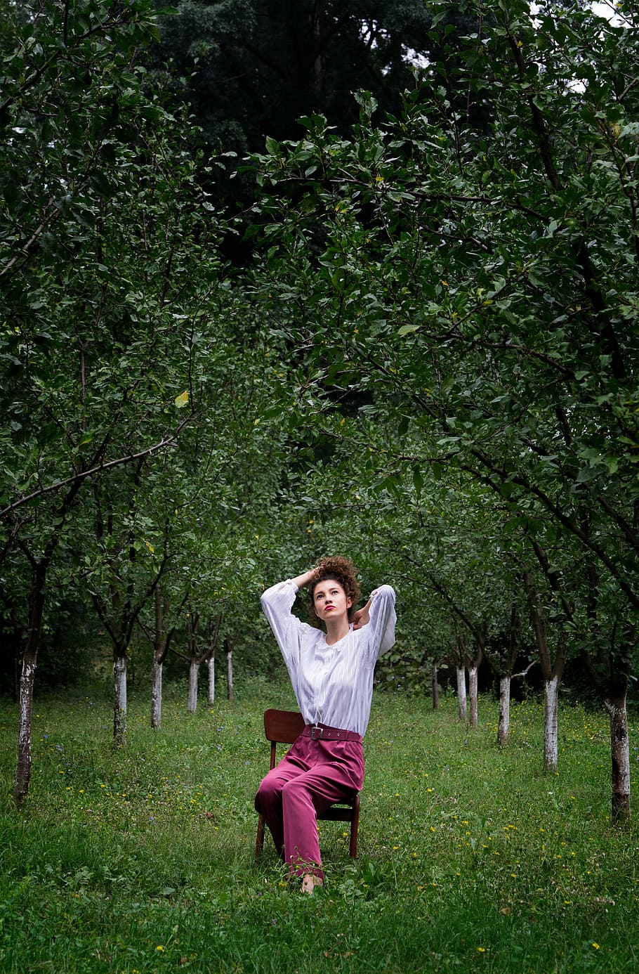 photo of woman in white long-sleeve top with red pants sitting on brown chair surround trees HD wallpaper