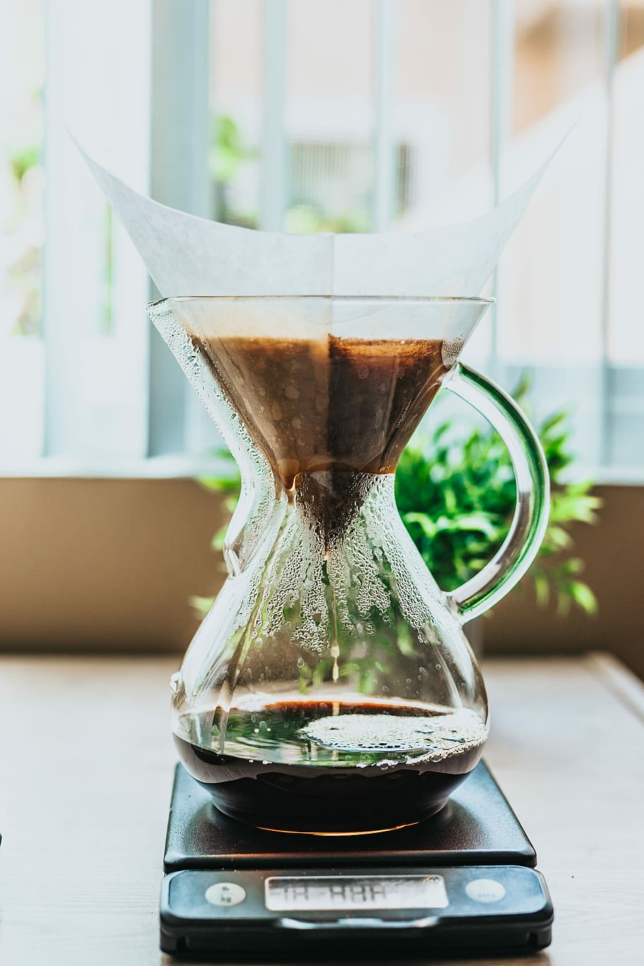 black pour-over coffeemaker on top of brown wood surface, coffee on clear glass pitcher