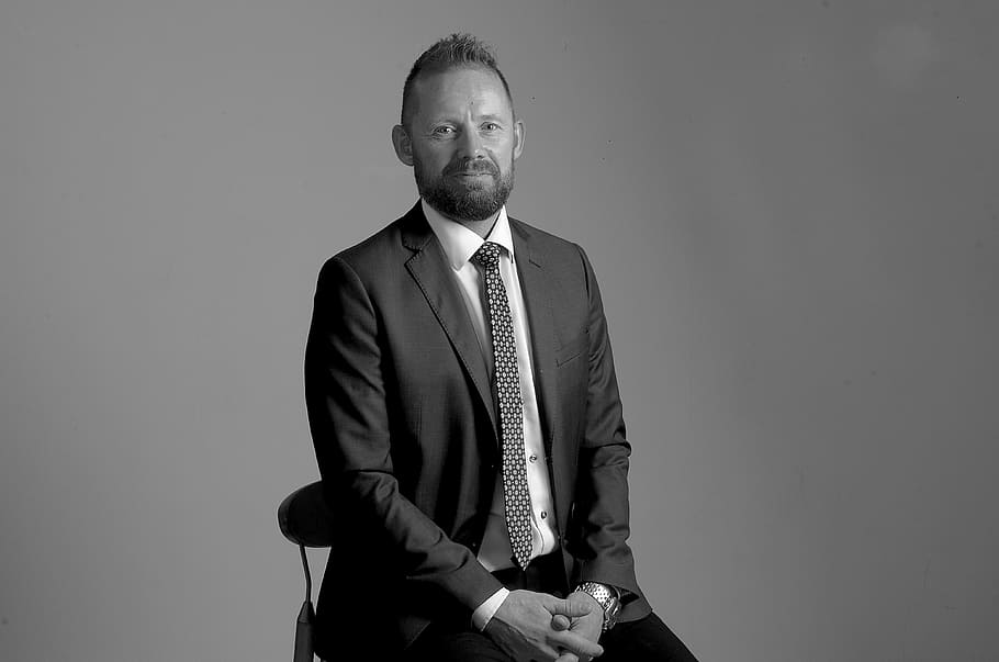 man sitting on chair, portrait, beard, smile, black and white HD wallpaper
