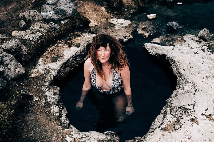 woman in cave wearing one-piece swimsuit looking upward, woman swimming on hot spring during daytime