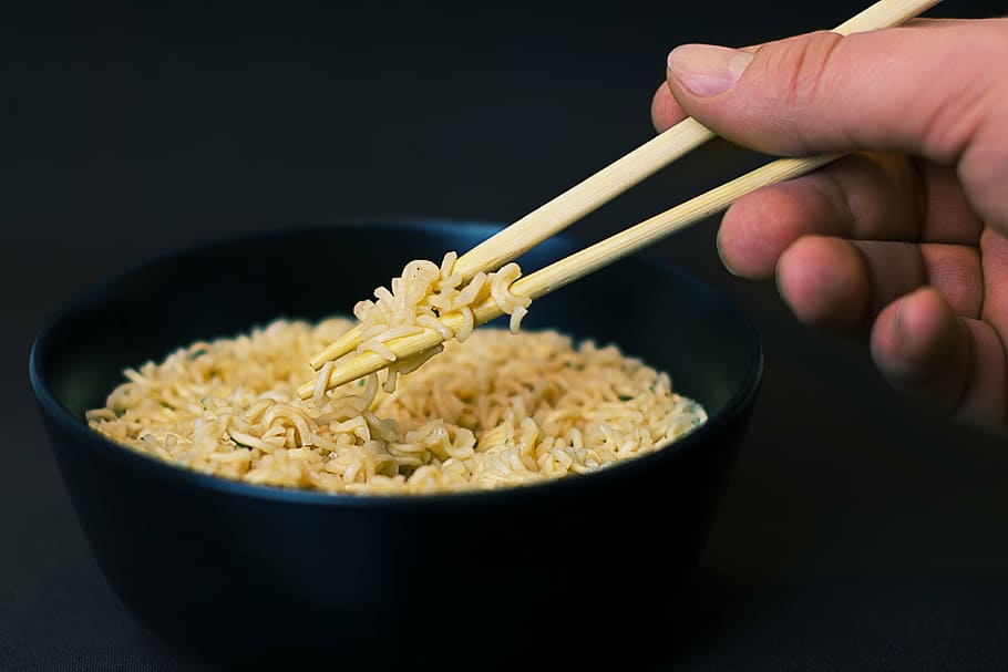 person eating noodles using chopsticks, holding, noddles, bowl