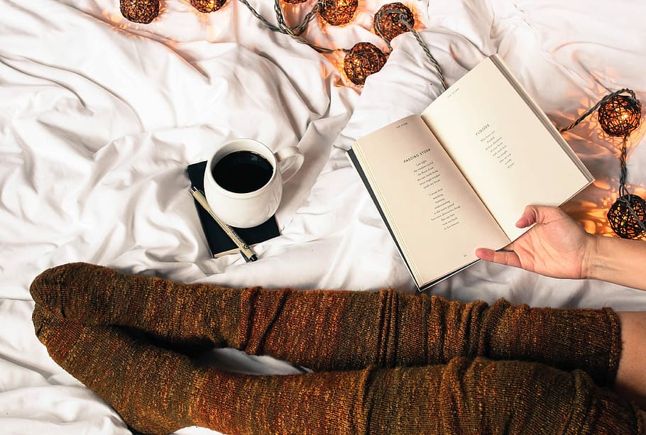 mug of black coffee beside person's feet wearing brown stockigns, person holding book near white ceramic mug HD wallpaper