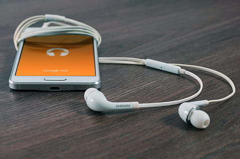 white Samsung Android smartphone turned beside white earbuds on brown board, turned on smartphone with earbuds HD wallpaper