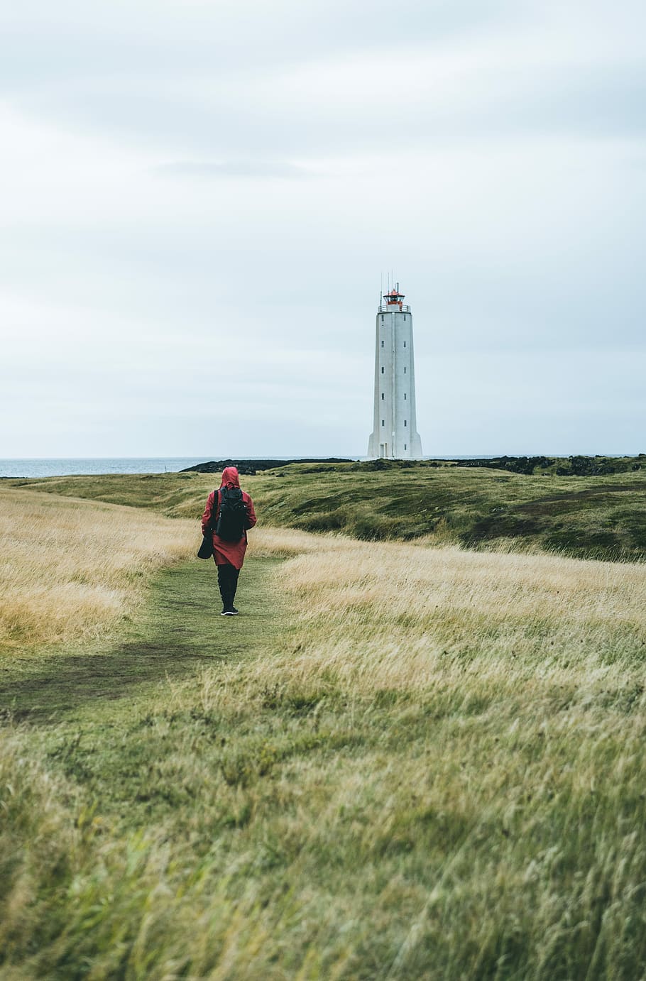 woman in red dress walks on green grass leading to white lighthouse, woman walking near white concrete building under white clouds during daytime HD wallpaper