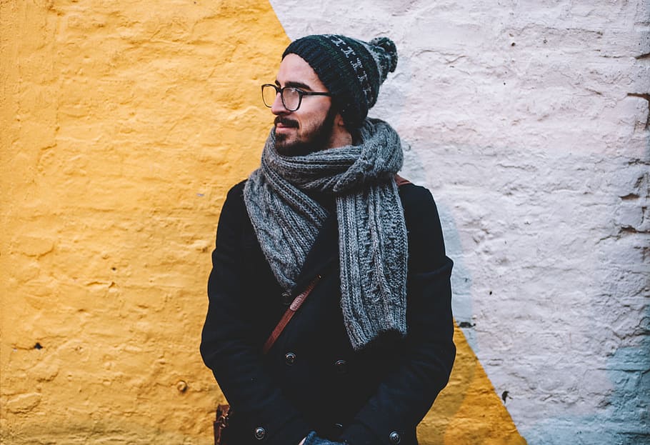 man in black coat with grey scarf standing on front of white and yellow painted wall, man in grey scarf leaning on wall, HD wallpaper