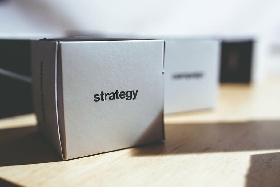 white Strategy box on brown wooden surface, typo, words, letters