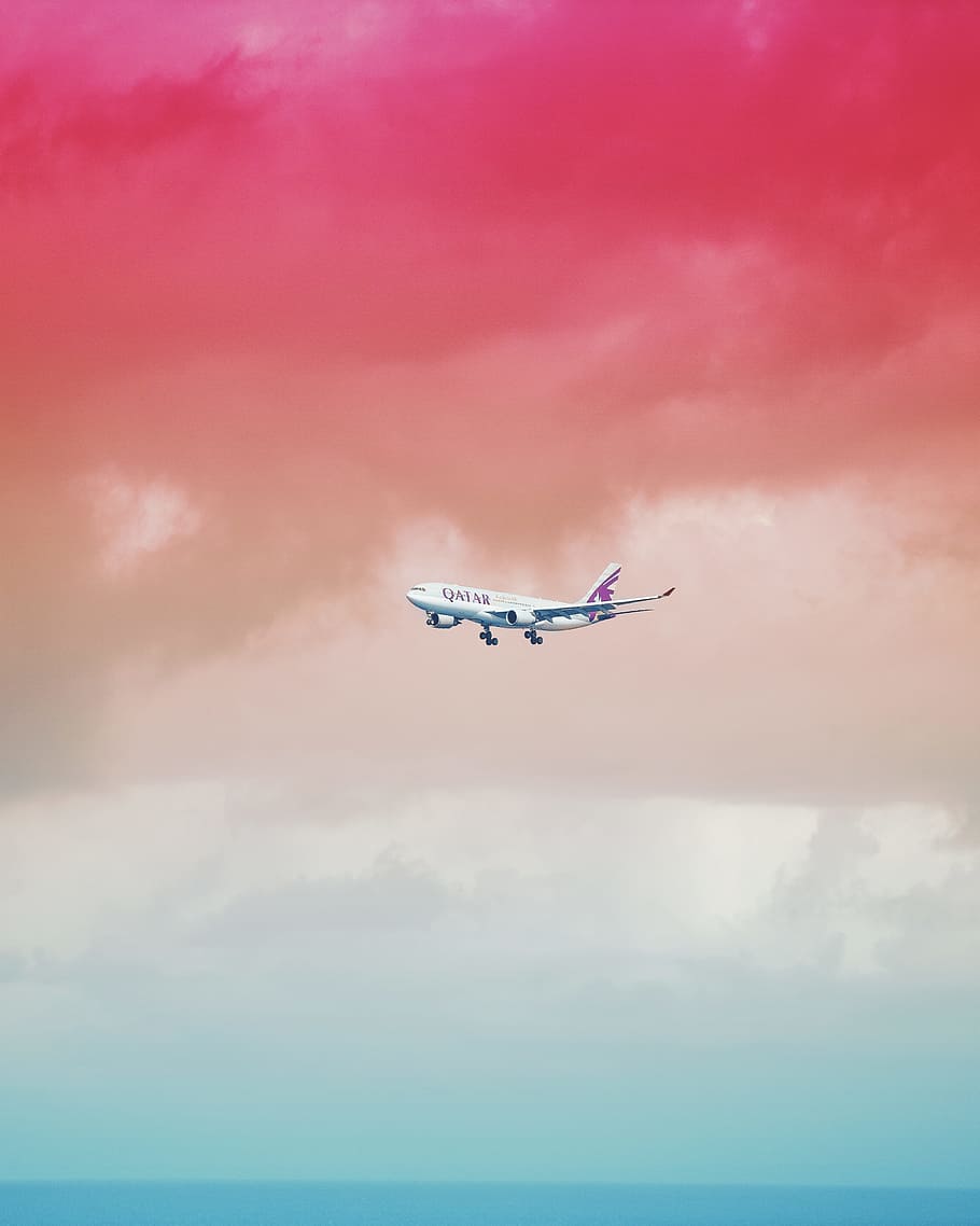 Qatar Airlines airplane flying under red cloud formation, white Qatar Airlines airplane below red and gray clouds