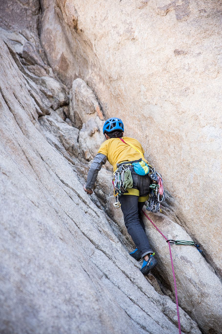 man wearing yellow climbing on cliff during daytime, person walking toward rocky mountain HD wallpaper