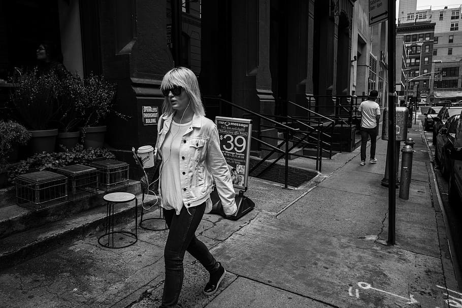 woman walking on pathway near concrete building, grayscale photo of woman walking on street