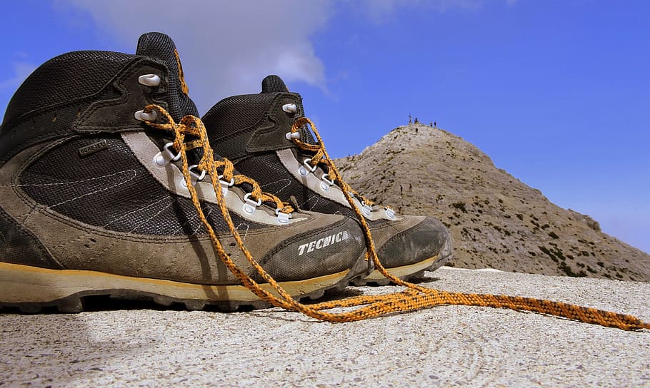 gray-and-brown hiking boots on gray sand overlooking brown hill under blue skies HD wallpaper