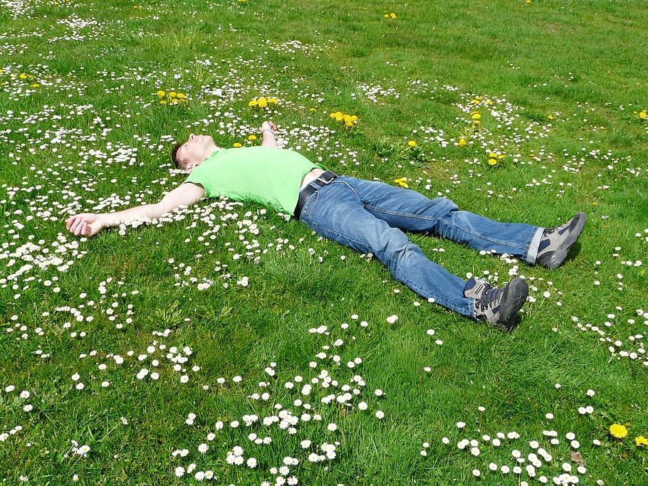 man lying open arms on grass field with flowers, rest, relax