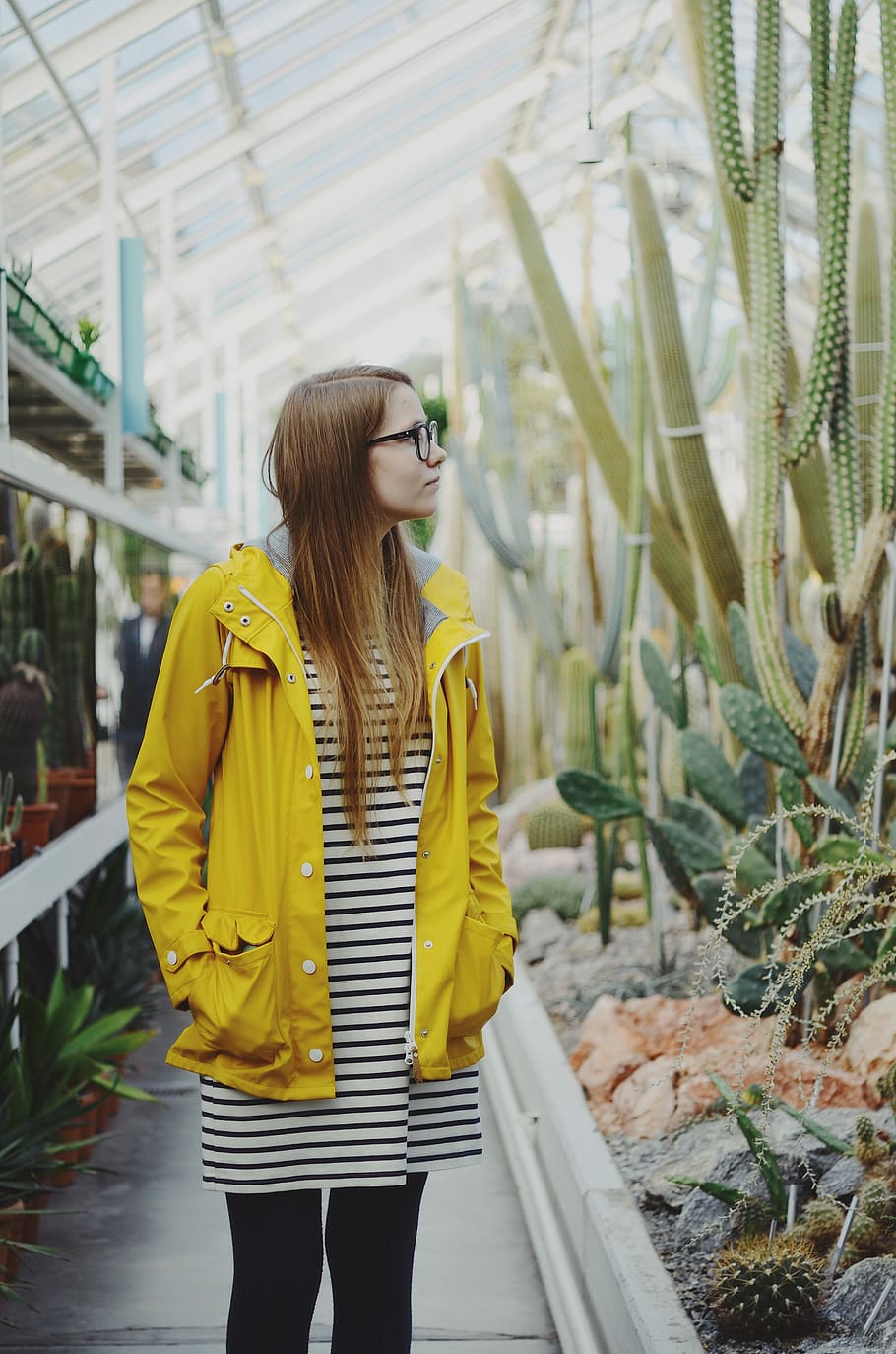woman wearing black and white striped dress and yellow jacket staring at plant