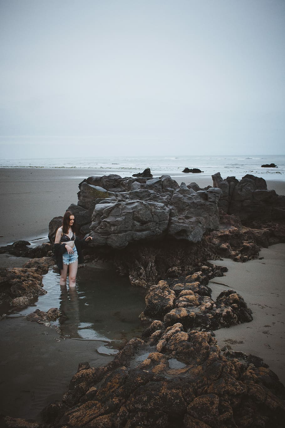 woman standing beside stone on beach shore, woman standing on body of water near rock HD wallpaper