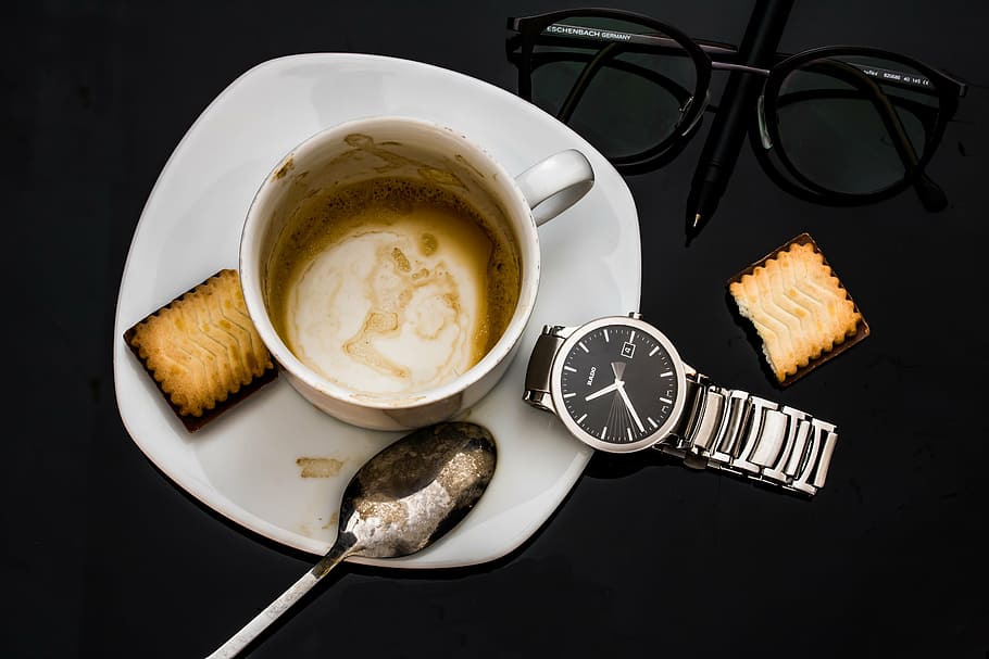 round black silver-colored watch near cup, empty coffee cup, dried coffee