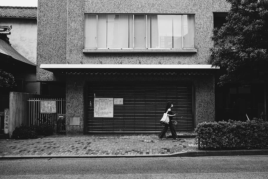 grayscale photo of woman walking beside building, woman walking beside house during daytime HD wallpaper