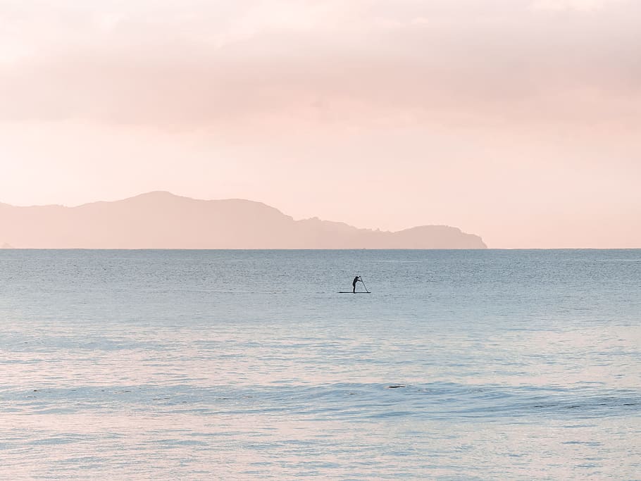 person paddle boarding during daytime, person standing on paddle board and rowing using a paddle on far distance