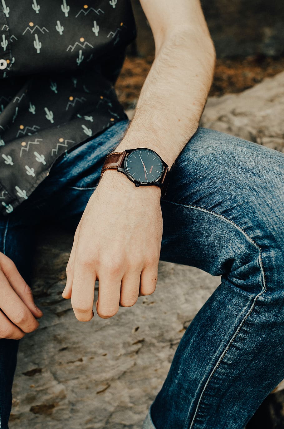 photo of person wearing analog watch and blue jeans and black top, man sitting on brown branch during daytime HD wallpaper
