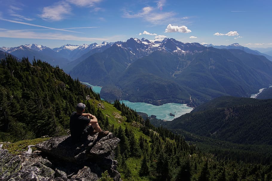 person sitting on rock formation facing landscape, man sitting on the cliff in front of hills HD wallpaper
