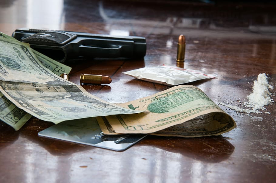 U.S. Dollar bills near black semi-automatic pistol on wooden surface