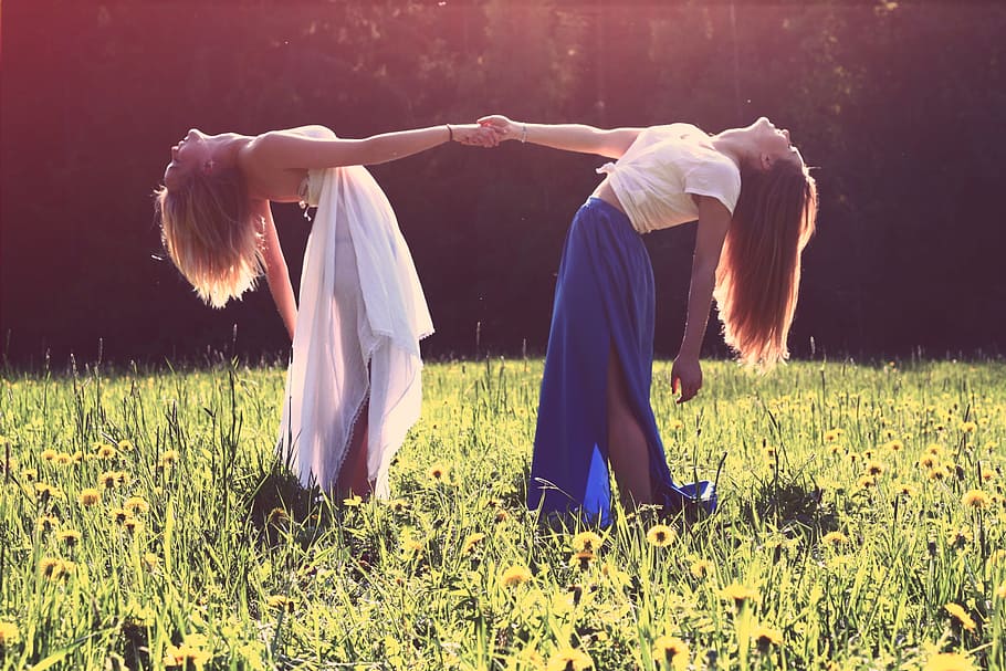 two women bending while holding hands, two women standing on green grass field while holding hands during daytime