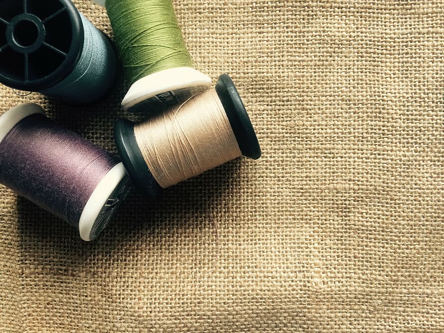 four assorted-color threads with spools over beige canvas textile HD wallpaper